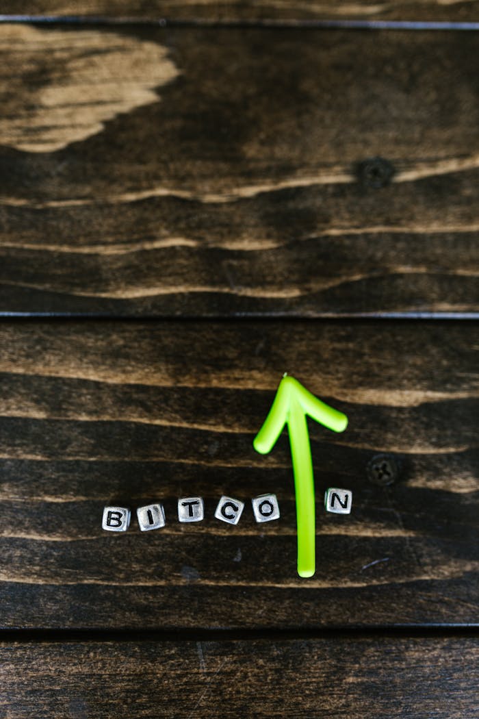 Green arrow and Bitcoin lettering on a wooden surface symbolize cryptocurrency growth.