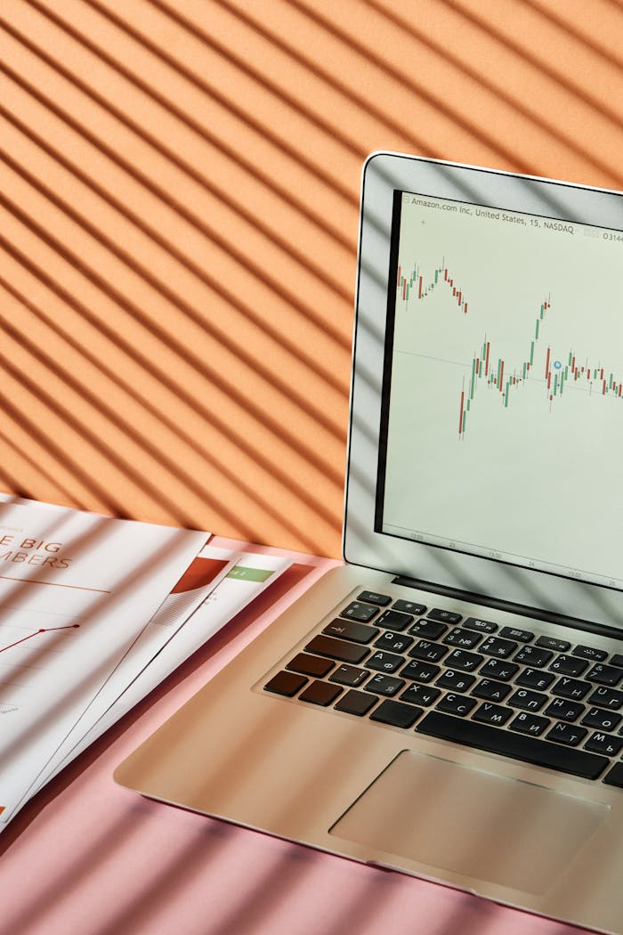 Laptop displaying stock market graph with shadows on desk, conveying a finance theme.